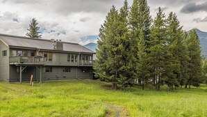 A two-story house with a balcony, surrounded by a grassy yard and tall trees.