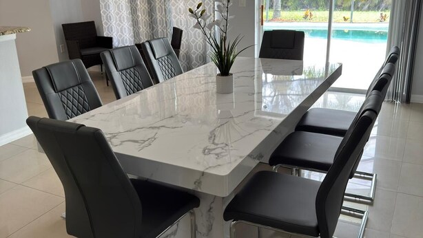 A modern dining area with a marble table, black chairs, and a view of a swimming pool. - Charming 3-bedroom house with WiFi, AC, Pool, Lake View, by Disney. (Kissimmee)