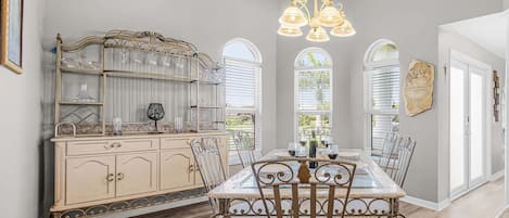 Un comedor con mesa de vidrio, sillas metálicas, un aparador decorativo y una araña.