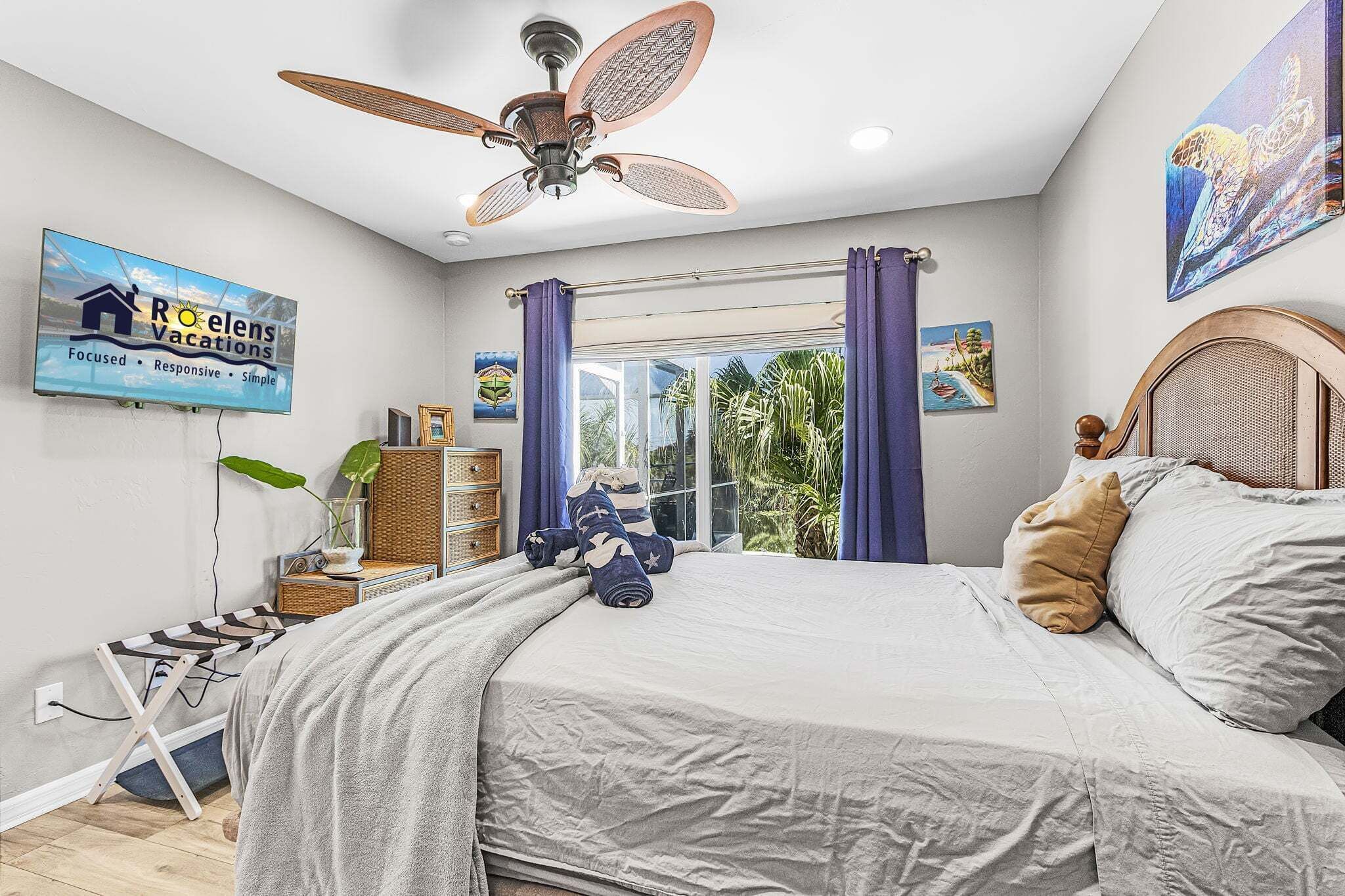 A bedroom with a bed, a ceiling fan, a TV, and a window with curtains.