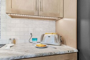 A kitchen with a toaster, a plate with toast, a glass of water, and salt and pepper shakers on the counter. - Unforgettable Moment Awaits - Shadroe Canal Villa  - Roelens (Cape Coral)
