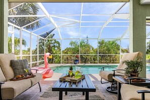 A glass-enclosed patio with a pool, outdoor furniture, and a flamingo decoration.