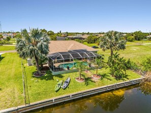 A house with a covered patio, a swimming pool, and a small dock with a kayak. - Unforgettable Moment Awaits - Shadroe Canal Villa  - Roelens (Cape Coral)