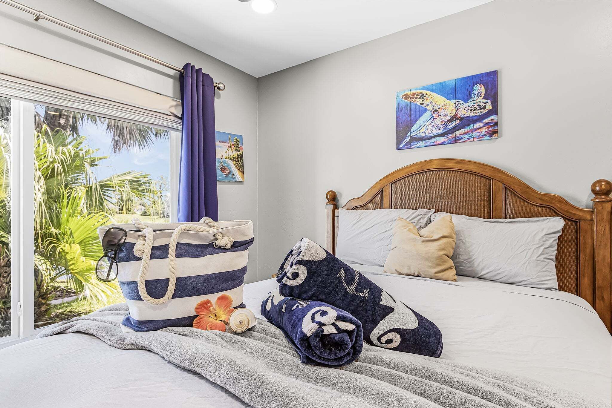 A bedroom with a bed, a window with curtains, a painting on the wall, and a bag on the bed.