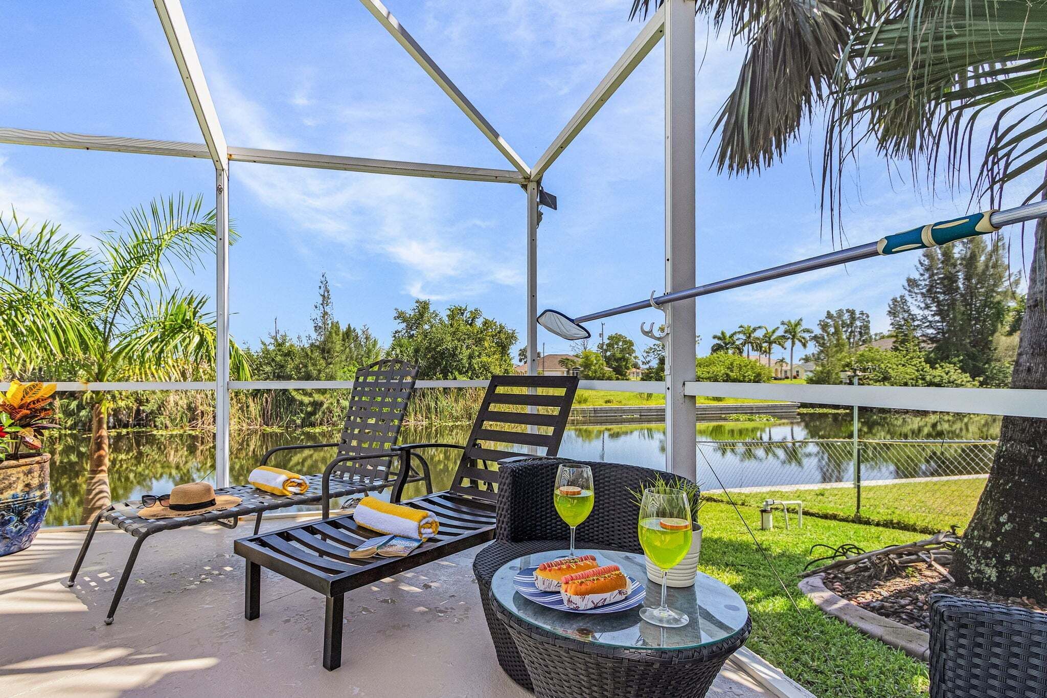 Un patio al aire libre con un área de estar cubierta, una mesa con comida y bebidas, y vistas a un cuerpo de agua y follaje.