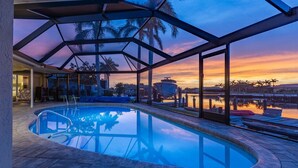 Une piscine entourée de parois en verre, un espace de détente et une vue sur un quai et l’eau.