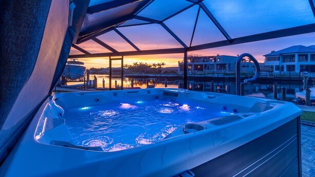 Un bain à remous avec vue sur un coucher de soleil se reflétant sur l’eau et les bâtiments.