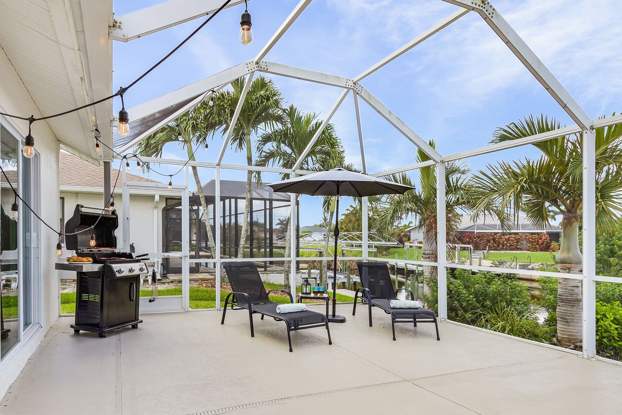 Une terrasse extérieure équipée d’un barbecue, de chaises longues et de parasols.