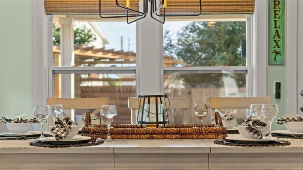 Un comedor con una mesa larga preparada para dos personas, un posavasos tejido y vistas al exterior a través de un ventanal.