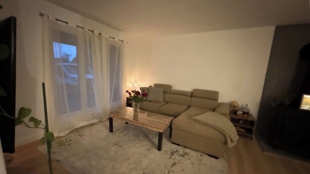 Un salón con un sofá color beige, una mesita de centro, una planta y una chimenea.
