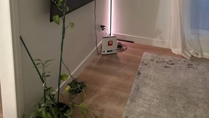Una habitación con un televisor de pantalla plana montado en la pared, una lámpara de pie y una planta en maceta.