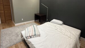 Un dormitorio con cama, mesita de noche, lámpara de pie, armario de madera y alfombra gris.