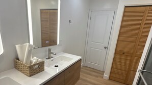 Un baño moderno con un espejo grande, encimeras blancas, armarios de madera y una puerta de madera.