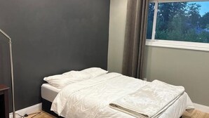 Un dormitorio con cama, ventana con cortinas, lámpara de pie y alfombra estampada.
