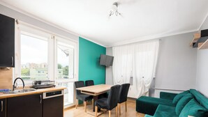 Une cuisine moderne avec un coin repas, un canapé vert et un téléviseur fixé au mur.