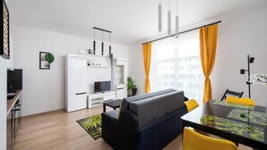 Un espace de vie moderne comprenant un canapé, une table à manger et des chaises, un coin cuisine et une grande fenêtre avec des rideaux.