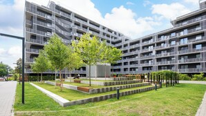 Un immeuble d’appartements moderne doté de nombreux balcons, d’une cour intérieure arborée et d’un chemin piétonnier dallé.