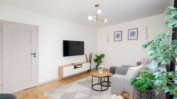 A modern living room with a flat-screen TV, a grey sofa, a coffee table, and a potted plant.