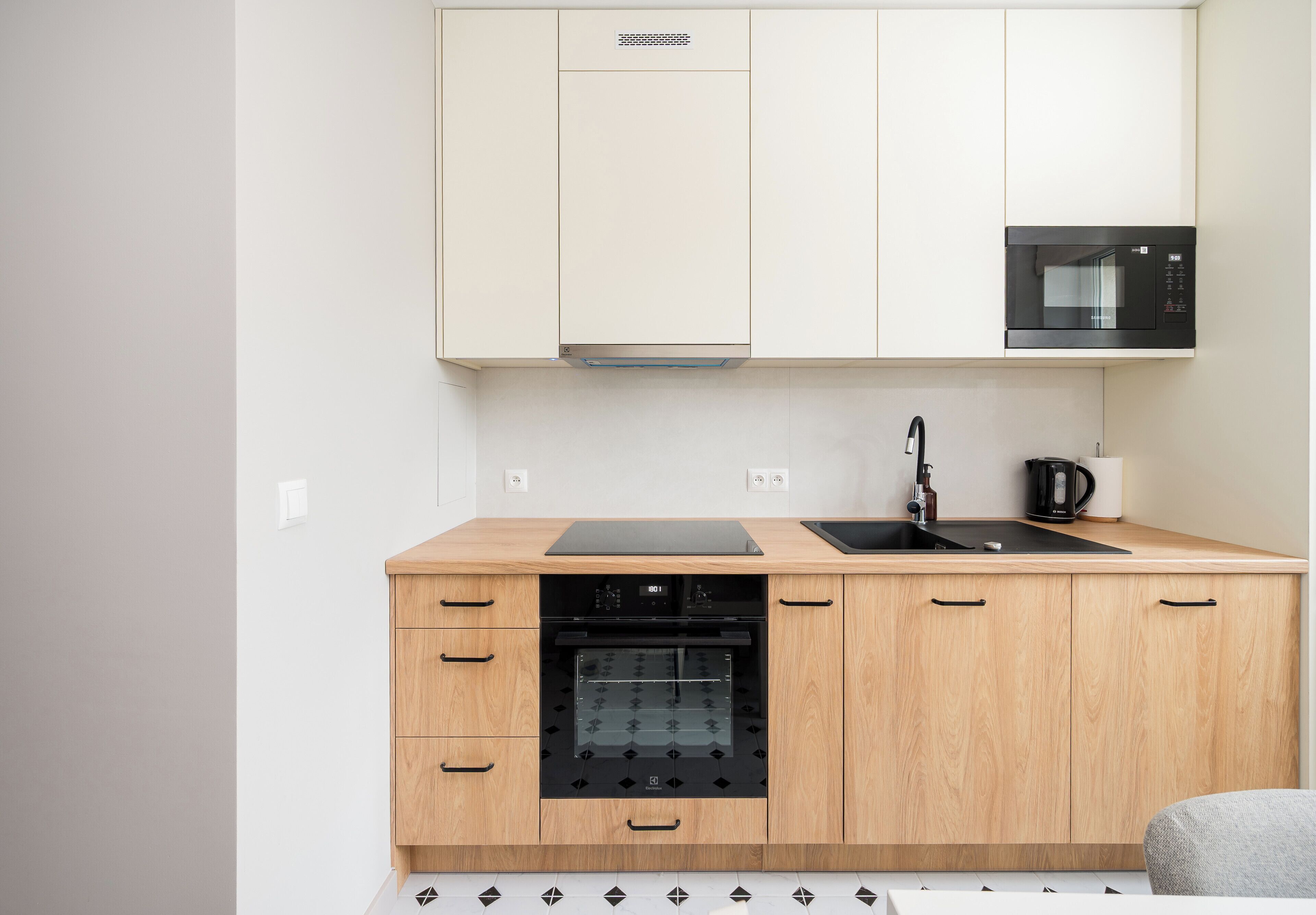 A modern kitchen with wooden cabinets, a built-in oven, a microwave, and a black countertop.