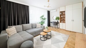 A modern living room with a grey sectional sofa, two small round tables, a wooden floor, and a large wardrobe. - Wrzeciono Comfortline Apartment (Warszawa)