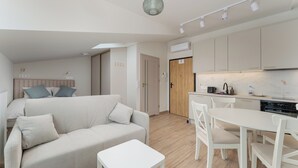 A modern, well-lit living room with a sofa, a small table, and a kitchen area with white cabinets and a dining table. - Kalwaryjska Elegant Stay Studio 18B (Kraków)