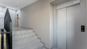 A modern elevator with a digital display, a staircase with grey tiles, and a minimalist wall design. - Kalwaryjska Elegant Stay Studio 18B (Kraków)