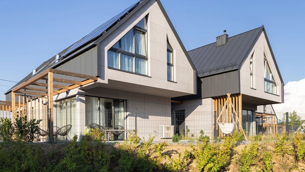 Ein modernes, zweistöckiges Haus mit Satteldach, großen Fenstern und einer sichtbaren Solaranlage.