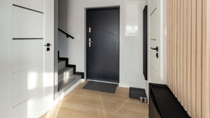 Ein moderner Flur mit einer dunklen Tür, einer Treppe und einer Holzvertäfelung auf der rechten Seite.