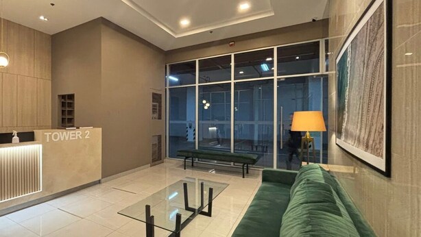 En moderne lobby med en receptionsdisk med teksten "TOWER 2", en grøn sofa, et glasbord og et stort vindue der giver udsigt over interiøret.