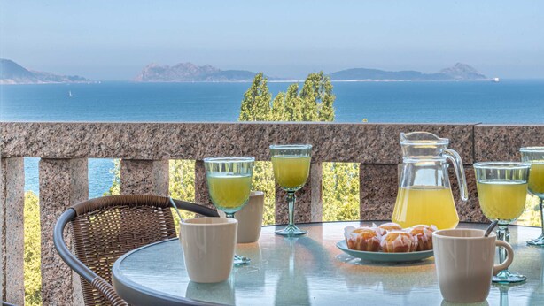 Una mesa con bebidas y pasteles en un balcón con vista al mar.