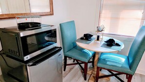 Une cuisine compacte équipée d’un four à micro-ondes, d’un petit réfrigérateur et d’une table à manger avec des chaises.