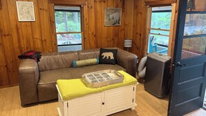Ein Zimmer mit einem braunen Ledersofa, einem weißen Schrank, Holzwänden und einer Tür, die nach draußen führt.