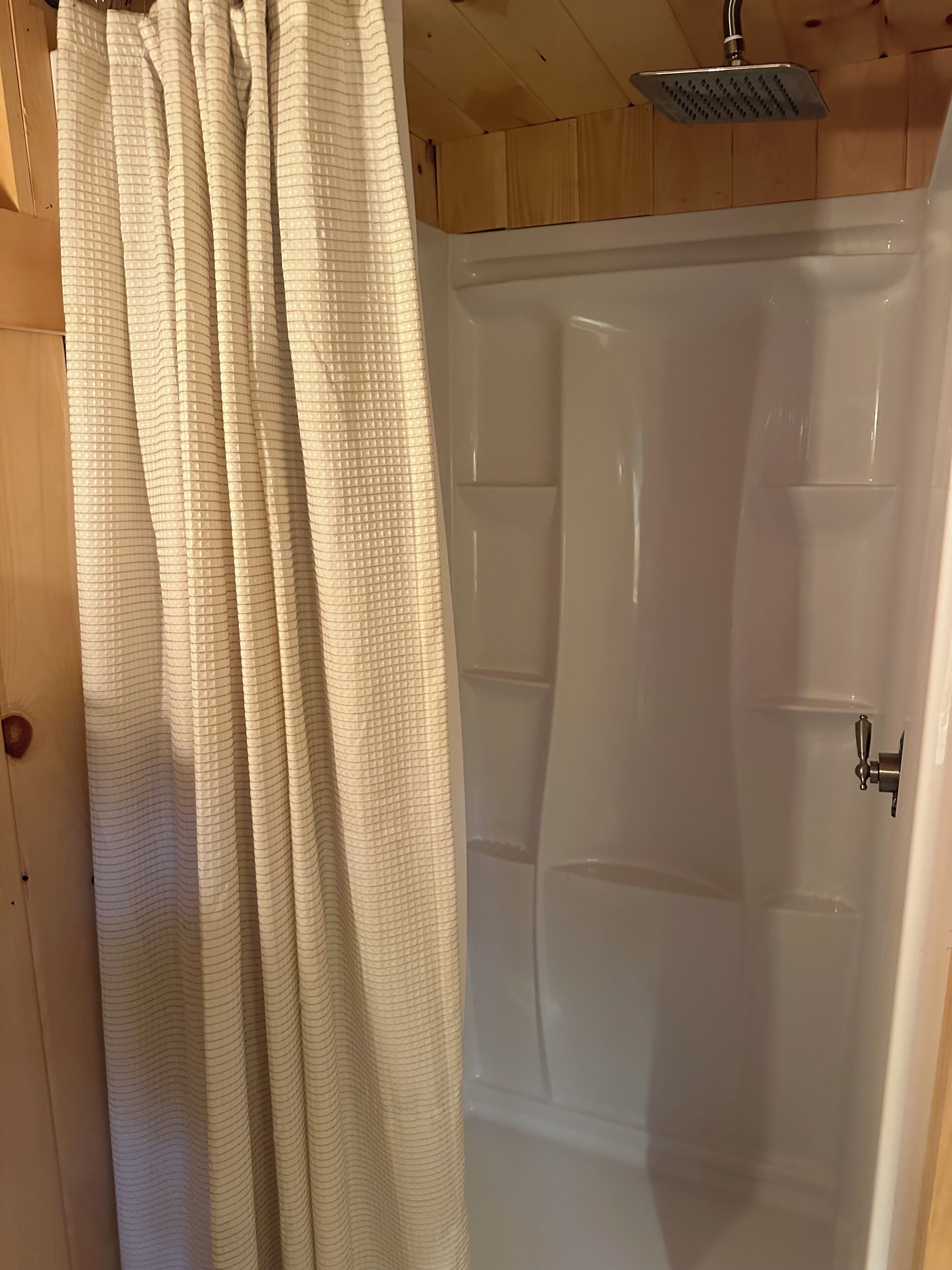 A wooden interior with a shower area featuring a white bathtub and a showerhead.