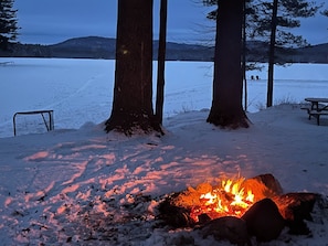 Lumipeitteinen maisema, jossa on nuotio, puita ja piknikpöytä.