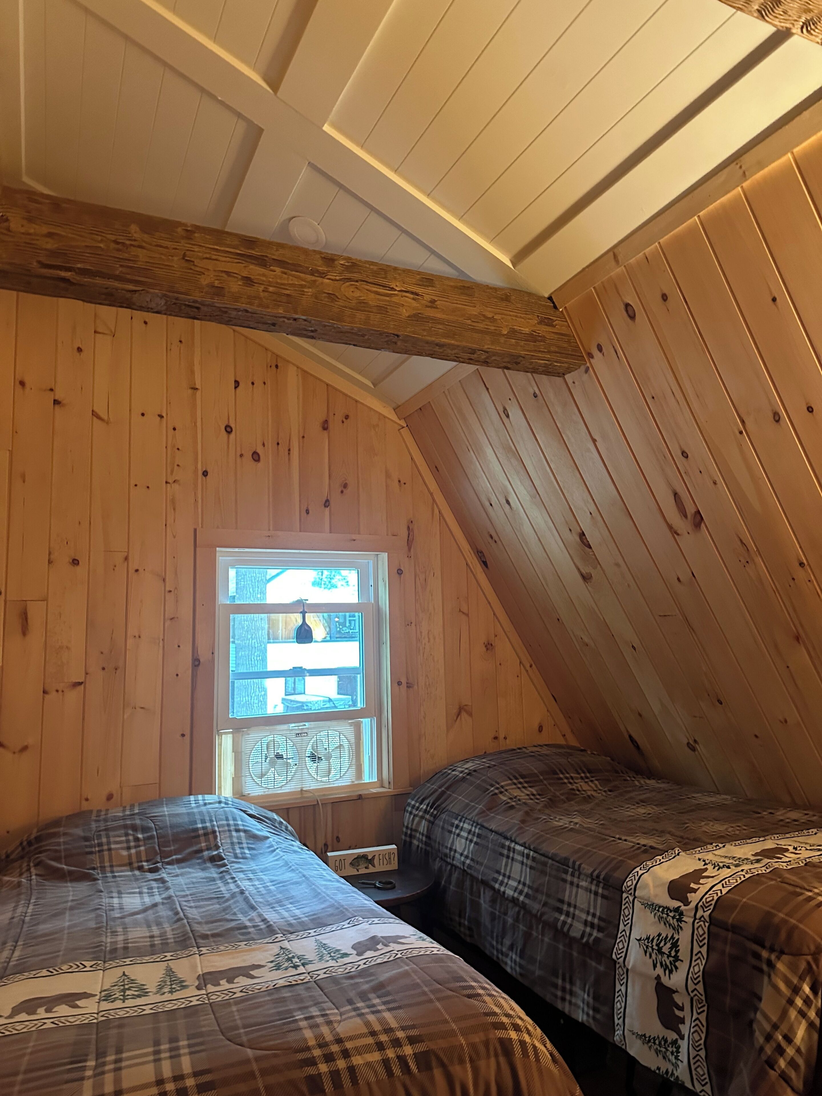 Une chambre avec deux lits, des murs en bois, un plafond en pente et une fenêtre équipée de climatiseurs.