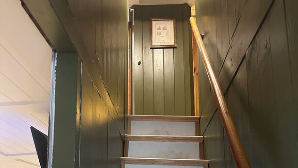 Eine Holztreppe mit Handlauf, die zu einer Tür führt, über der sich ein gerahmtes Bild befindet.