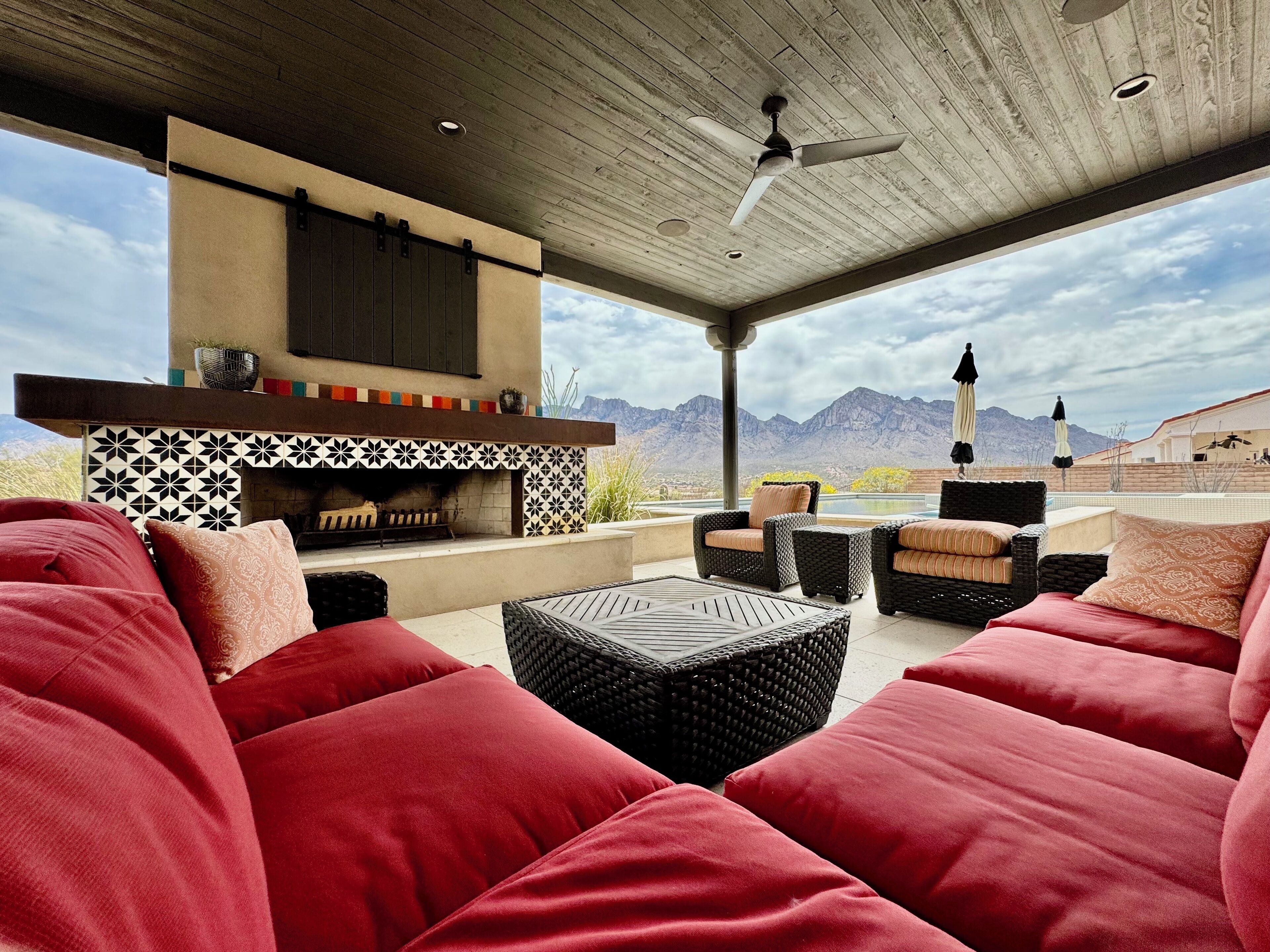 Un patio exterior con sofás rojos, una chimenea y vistas a montañas.