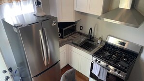 A compact kitchen with a stainless steel refrigerator, a gas stove, a microwave, and white cabinetry. - Charming 1-bedroom house in fabulous Hamburg (Hamburg)