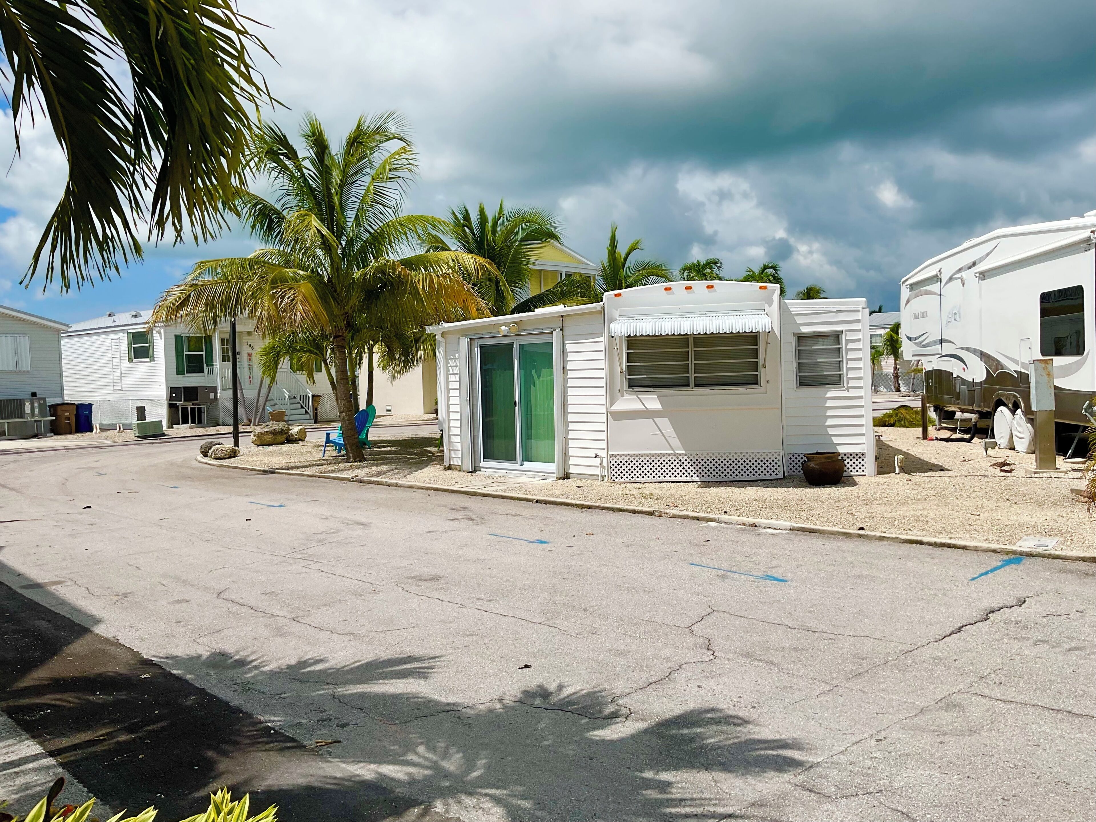 Una casa móvil con puerta verde, una estructura pequeña adosada y una caravana estacionada cerca.