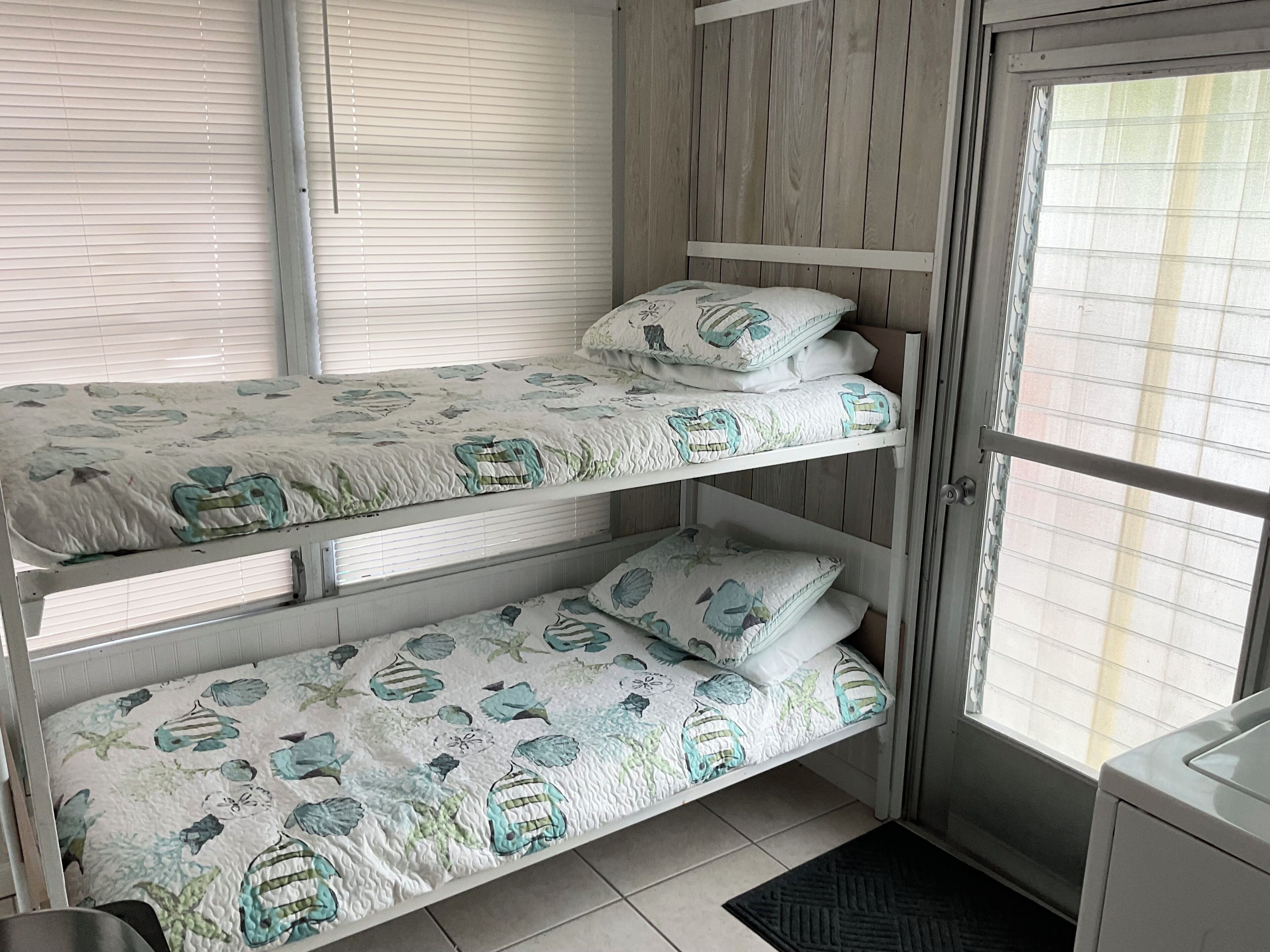 Uma cama beliche com roupa de cama florida, uma parede de madeira e uma janela com persianas.