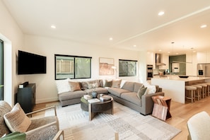 A modern living room with a sectional sofa, a coffee table, and a flat-screen TV mounted on the wall.