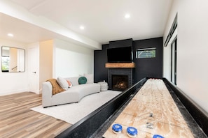 A modern living room with a fireplace, a sofa, and a shuffleboard table.