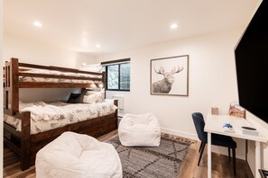 Una cama litera con escritorio y silla, una alfombra y un cuadro con una imagen de animales en una habitación con paredes blancas.