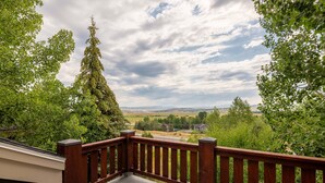 A balcony with a wooden railing overlooking a landscape with trees and a distant view of houses.