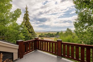 A balcony with a wooden railing overlooking a landscape with trees and a distant view of houses.