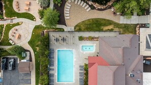 An aerial view of a residential property with a swimming pool, patio seating, and a parking area.