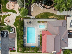 An aerial view of a residential property with a swimming pool, patio seating, and a parking area.