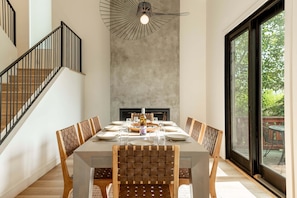 Un coin repas avec une table dressée pour six personnes, une cheminée et un escalier.
