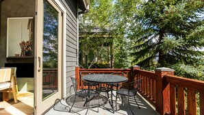 A covered patio with a round table and chairs, a wooden deck, and a view of trees and a building. - Bear Hollow Basecamp, Hot Tub, Balconies, Pool Clubhouse (Park City)