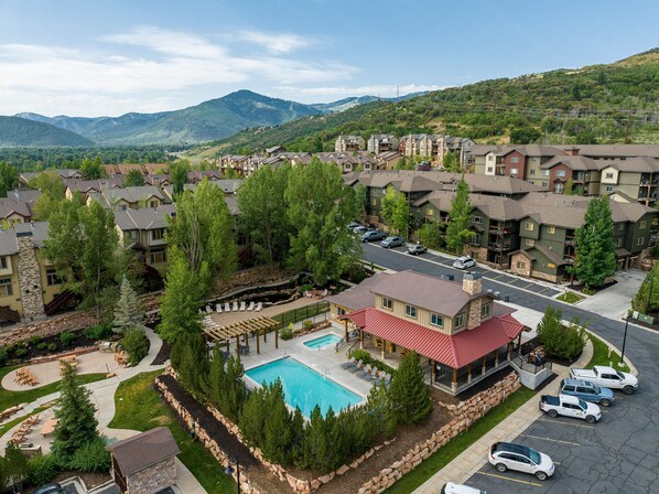 A residential area with a swimming pool, multiple-story buildings, and a mountainous backdrop.